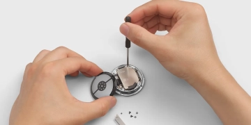 Hands disassembling a Google Pixel Watch 4 with a screwdriver to replace its battery, showing the watch's serviceable design