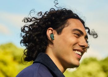 Man smiling outdoors wearing a green Fairphone Fairbuds 2 earbud