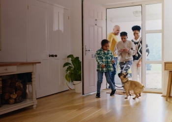 Family entering a hallway with a Google Nest speaker on a side table, Google Home