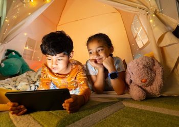 Two children in a glowing tent, one holding a tablet and one wearing a blue smartwatch, from Verizon's family perks announcement